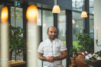 John Kasraei, P&auml;chter und Koch, steht im Wintergarten der Gastronomie Element in Kochjacke, die H&auml;nde vor dem Bauch.