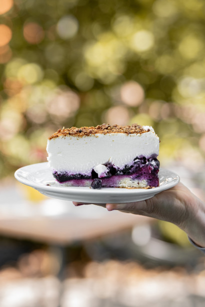 Hand h&auml;lt einen Quarkkuchen mit Blaubeeren, dar&uuml;ber Quarkschicht und Crunch.