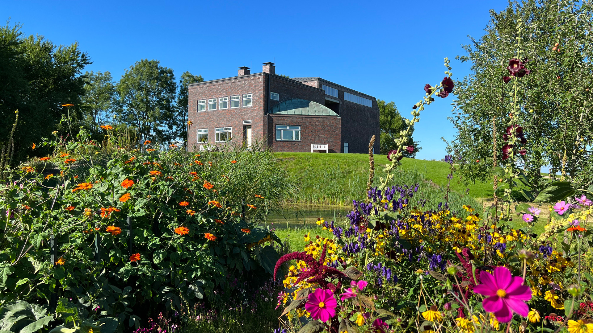 Nolde-huset i Seebüll med Fething og Nolde-haven i forgrunden under en blå himmel.