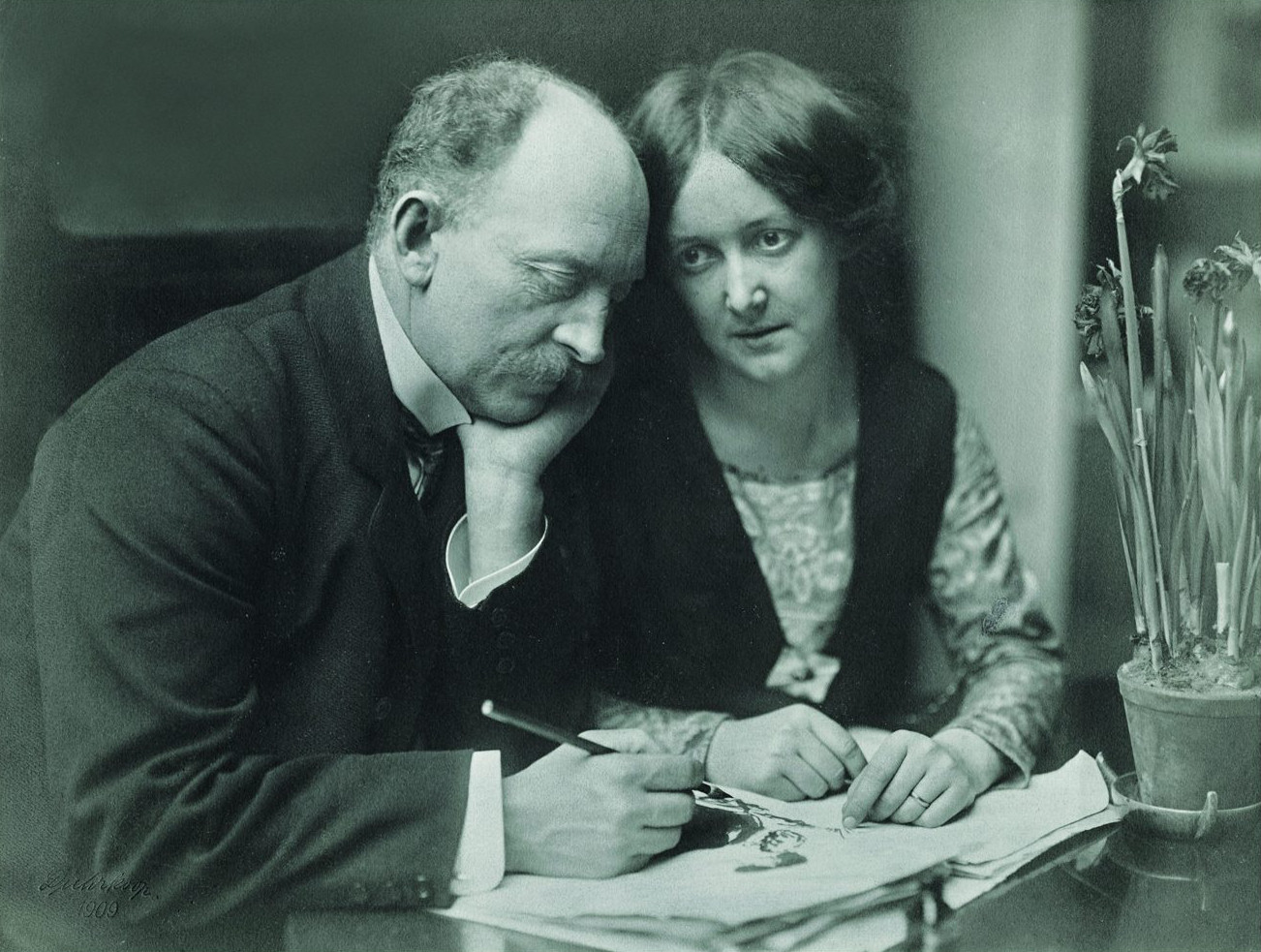 Historisches Foto von Ada und Emil Nolde, nebeneinander am Tisch sitzend; Emil Nolde mit Tintenfüller und Papieren vor sich.