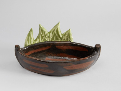 Keramikfigur in Form eines braunen Bootes mit gr&uuml;nem Schilf, Glasur in kr&auml;ftigen Braun- und Gr&uuml;nt&ouml;nen.