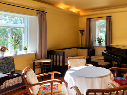 Bright yellow living room in the Nolde House with original furnishings, including a round table, chairs, sofa, armchair, and grand piano.
