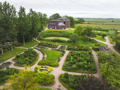 Luftfoto af Nolde-huset med gr&oslash;n have og det vidtstrakte marskomr&aring;de p&aring; en lys, skyet dag i sen for&aring;rstid.